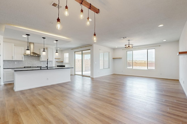 3034 Shannon Ln NE, Rio Rancho, NM 87144 - kitchen featuring wall chimney exhaust hood, dark countertops, open floor plan, white cabinetry, and light wood-type flooring