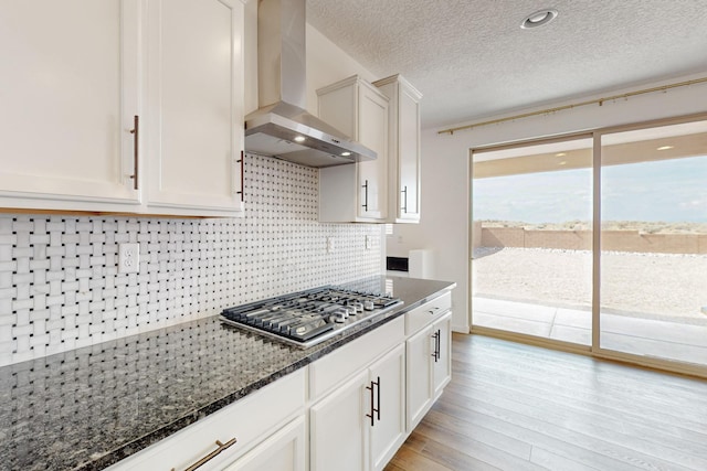 3034 Shannon Ln NE, Rio Rancho, NM 87144 - kitchen with wall chimney exhaust hood, stainless steel gas stovetop, light wood-style flooring, decorative backsplash, and dark stone countertops