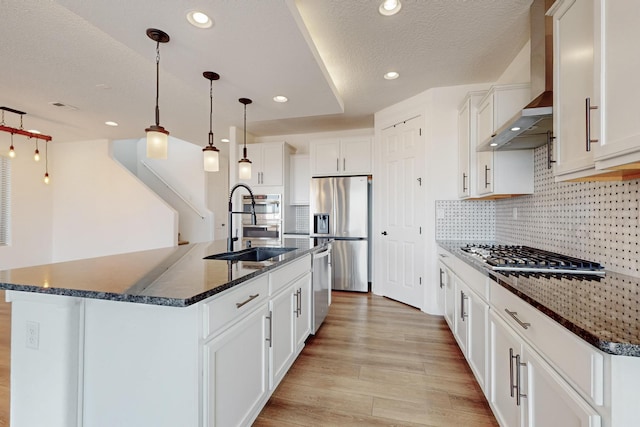 3034 Shannon Ln NE, Rio Rancho, NM 87144 - kitchen with wall chimney exhaust hood, appliances with stainless steel finishes, a sink, light wood finished floors, and a kitchen island with sink