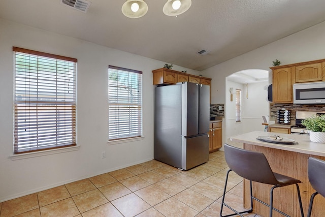 1034 Wagon Trail St, Los Lunas, NM 87031 - kitchen with appliances with stainless steel finishes, arched walkways, decorative backsplash, light countertops, and light tile patterned floors