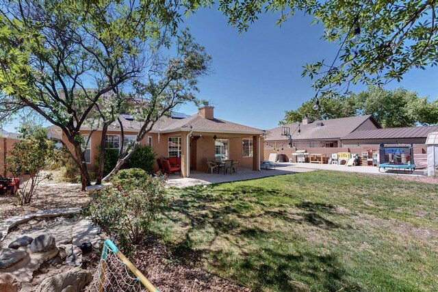 1034 Wagon Trail St, Los Lunas, NM 87031 - rear view of house featuring roof mounted solar panels, a patio area, stucco siding, a fenced backyard, and a chimney