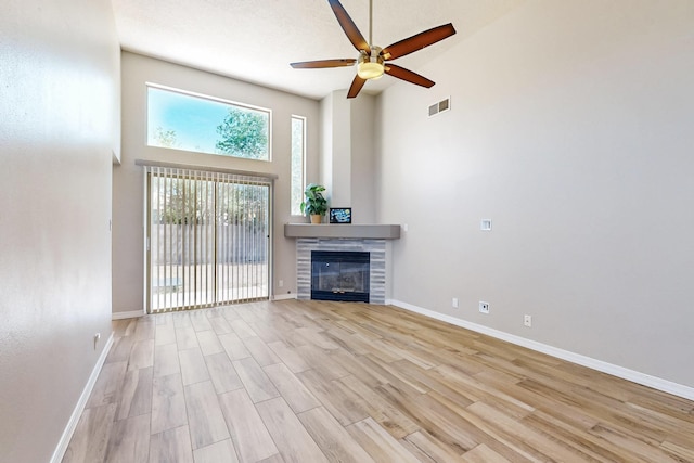 10809 Academy Ridge Rd NE, Albuquerque, NM 87111 - unfurnished living room featuring a towering ceiling, a ceiling fan, light wood-style flooring, a tiled fireplace, and baseboards