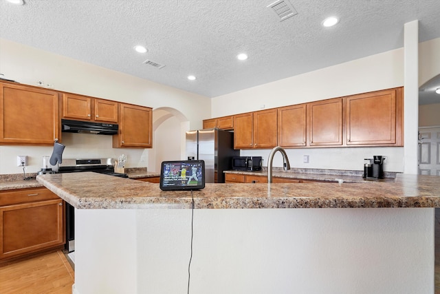 1311 Mirador Loop NE, Rio Rancho, NM 87144 - kitchen with under cabinet range hood, brown cabinets, stainless steel appliances, a textured ceiling, and light wood finished floors