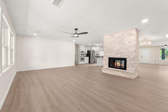 697 W Meadowlark Ln, Corrales, NM 87048 - unfurnished living room with ceiling fan, a fireplace, light wood-type flooring, baseboards, and a textured ceiling