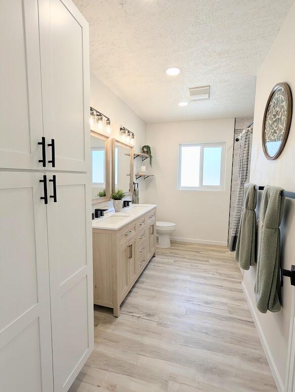 2824 Texas St NE, Albuquerque, NM 87110 - bathroom featuring a textured ceiling, vanity, baseboards, toilet, and wood finished floors
