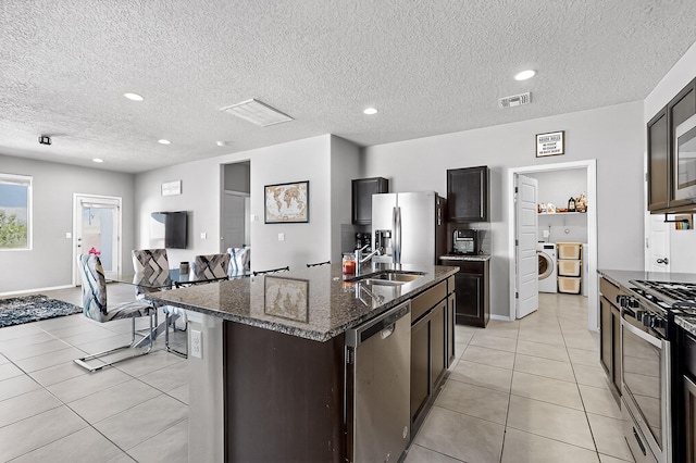 4871 Longs Peak Rd NE, Rio Rancho, NM 87144 - kitchen featuring stainless steel appliances, light tile patterned floors, dark stone countertops, a textured ceiling, and a kitchen island with sink