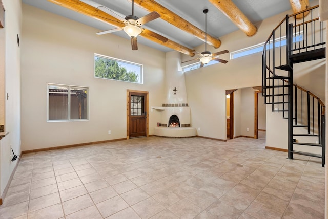 98 Edgewood Unit 7, Edgewood, NM 87015 - unfurnished living room with ceiling fan, a towering ceiling, a lit fireplace, light tile patterned flooring, and stairs