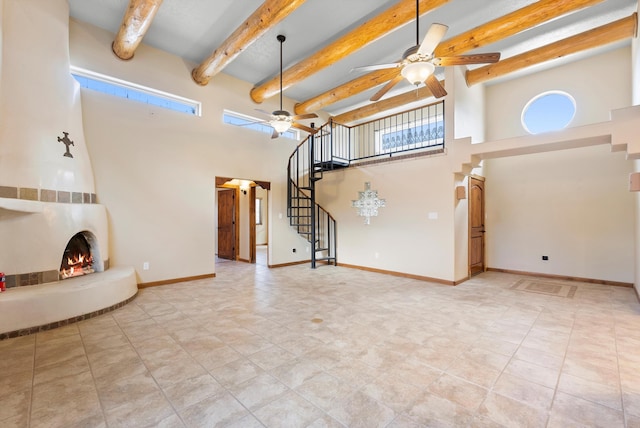 98 Edgewood Unit 7, Edgewood, NM 87015 - unfurnished living room featuring ceiling fan, a high ceiling, stairs, a lit fireplace, and beam ceiling