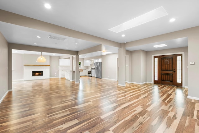 8320 Cherry Hills Dr NE, Albuquerque, NM 87111 - unfurnished living room with light wood-style floors, baseboards, a warm lit fireplace, recessed lighting, and a skylight