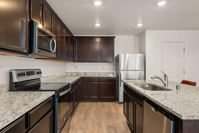 2425 Desi Loop, Belen, NM 87002 - kitchen featuring appliances with stainless steel finishes, a sink, light wood-style floors, light stone counters, and dark brown cabinetry