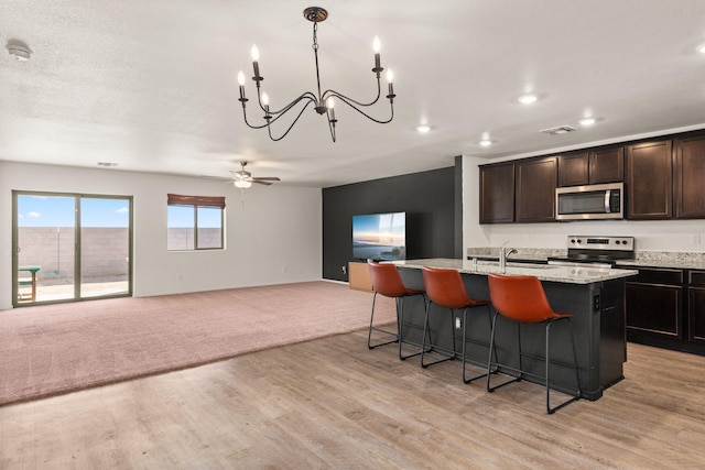 2425 Desi Loop, Belen, NM 87002 - kitchen with stainless steel appliances, open floor plan, a center island with sink, a kitchen bar, and a chandelier