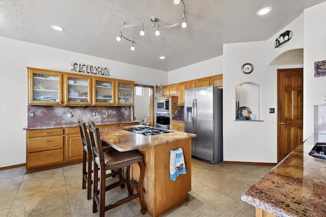 3039 Ashkirk Loop SE, Rio Rancho, NM 87124 - kitchen with appliances with stainless steel finishes, brown cabinets, baseboards, a center island, and a textured ceiling