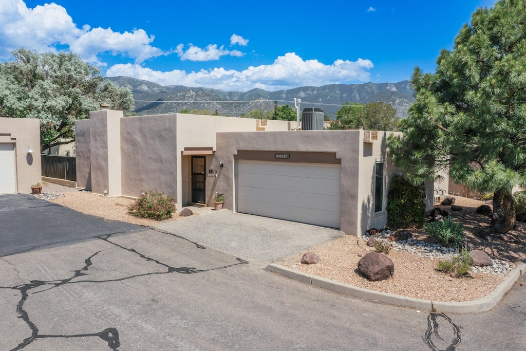 2403 Tramway Terrace Ct NE, Albuquerque, NM 87122 - pueblo-style house featuring a mountain view, a garage, central AC unit, and stucco siding