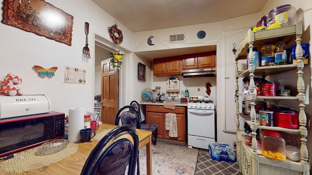 1207 Barelas Rd SW 1203, Albuquerque, NM 87105 - kitchen featuring white gas stove, under cabinet range hood, light countertops, and brown cabinets