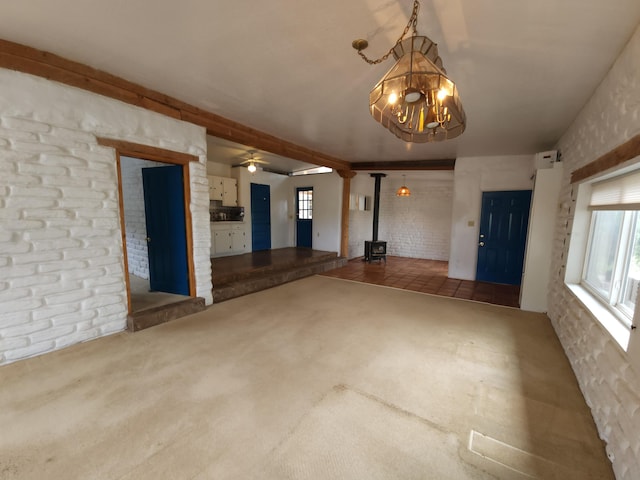 83 Paseo De San Antonio Rd, Placitas, NM 87043 - unfurnished living room featuring a wood stove, a chandelier, carpet floors, brick wall, and ceiling fan