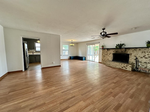 3901 70th St NW, Albuquerque, NM 87120 - unfurnished living room with a textured ceiling, a ceiling fan, light wood-type flooring, a brick fireplace, and baseboards