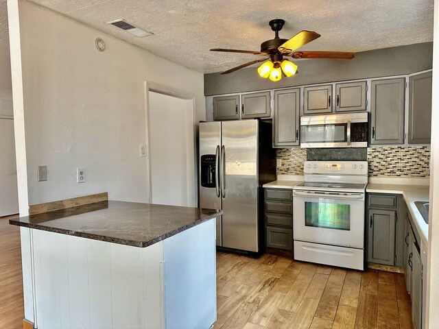 3901 70th St NW, Albuquerque, NM 87120 - kitchen with appliances with stainless steel finishes, light wood finished floors, a peninsula, decorative backsplash, and a textured ceiling