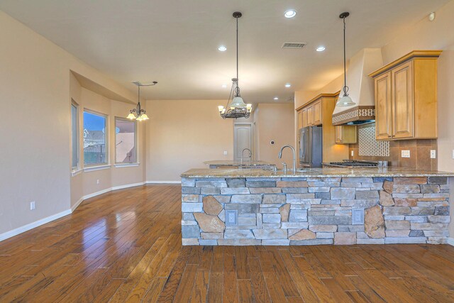 1624 23rd Ave SE, Rio Rancho, NM 87124 - kitchen featuring a chandelier, appliances with stainless steel finishes, wall chimney range hood, dark wood-style flooring, and light stone counters