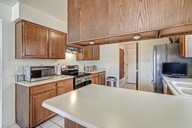 12323 Haines Ave NE, Albuquerque, NM 87112 - kitchen featuring appliances with stainless steel finishes, under cabinet range hood, a peninsula, light tile patterned floors, and light countertops