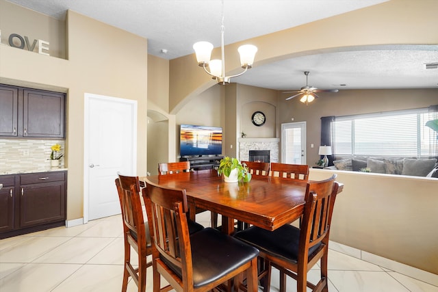8031 Corn Mountain Pl NW, Albuquerque, NM 87114 - dining room featuring ceiling fan, a tiled fireplace, vaulted ceiling, arched walkways, and light tile patterned flooring