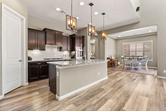 4118 Pico Norte Ln NE, Rio Rancho, NM 87124 - kitchen featuring light wood finished floors, a chandelier, dark brown cabinetry, a textured ceiling, and decorative backsplash