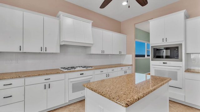4281 Palo Verde Ct, Los Lunas, NM 87031 - kitchen featuring white appliances, ceiling fan, a kitchen island, light tile patterned flooring, and white cabinetry