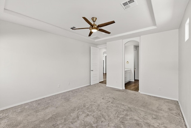 215 Adeline Ave, Los Lunas, NM 87031 - unfurnished bedroom with a tray ceiling, dark carpet, arched walkways, ensuite bath, and a ceiling fan