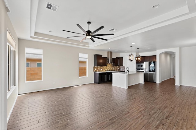 275 Adeline Ave, Los Lunas, NM 87031 - unfurnished living room with a tray ceiling, ceiling fan, dark wood-style flooring, arched walkways, and recessed lighting