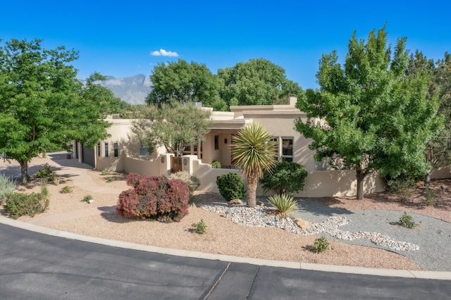 317 Plaza Muchomas, Bernalillo, NM 87004 - pueblo revival-style home with stucco siding, a garage, a chimney, a mountain view, and a fenced front yard