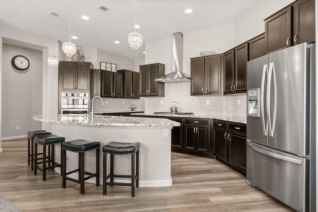 9128 Vista Bosquejo Rd NW, Albuquerque, NM 87120 - kitchen featuring stainless steel appliances, wall chimney exhaust hood, light wood finished floors, backsplash, and a kitchen bar