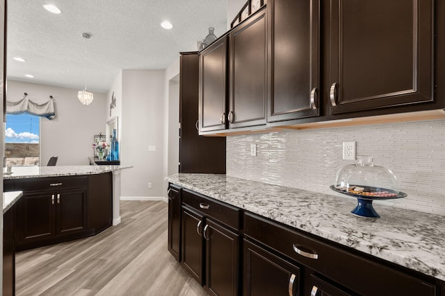 9128 Vista Bosquejo Rd NW, Albuquerque, NM 87120 - kitchen featuring light wood finished floors, tasteful backsplash, dark brown cabinets, light stone countertops, and a textured ceiling