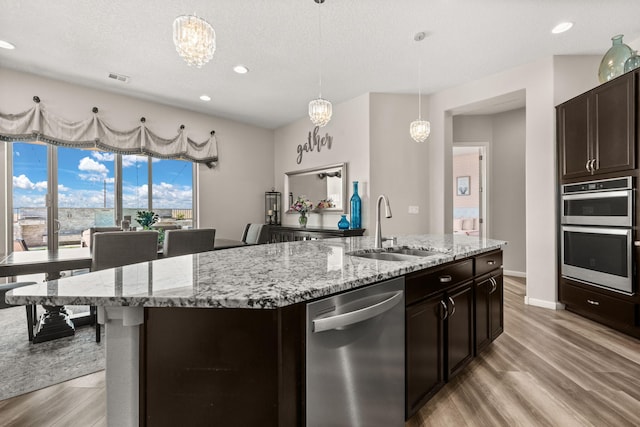 9128 Vista Bosquejo Rd NW, Albuquerque, NM 87120 - kitchen with stainless steel appliances, light wood-style flooring, light stone countertops, an island with sink, and hanging light fixtures