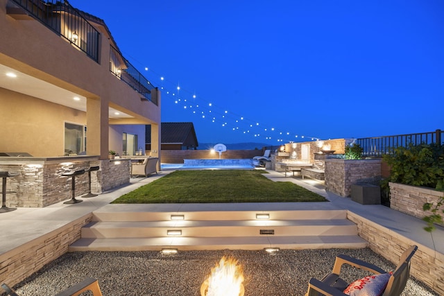9128 Vista Bosquejo Rd NW, Albuquerque, NM 87120 - yard at twilight featuring a fire pit, exterior kitchen, a fenced backyard, a bar, and a patio