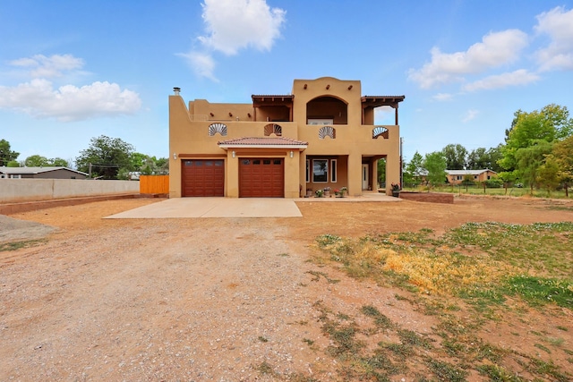 2061 Blaylock Ln NE, Los Lunas, NM 87031 - pueblo-style home with a balcony, driveway, stucco siding, and a garage