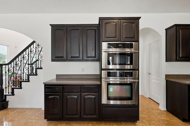 2061 Blaylock Ln NE, Los Lunas, NM 87031 - kitchen with double oven, arched walkways, dark brown cabinetry, dark countertops, and light tile patterned floors