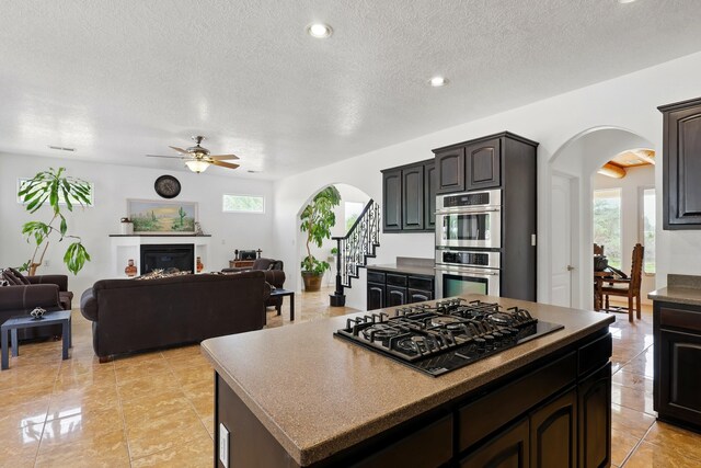 2061 Blaylock Ln NE, Los Lunas, NM 87031 - kitchen featuring arched walkways, black gas cooktop, stainless steel double oven, a ceiling fan, and a textured ceiling