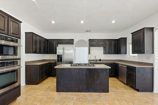 2061 Blaylock Ln NE, Los Lunas, NM 87031 - kitchen with appliances with stainless steel finishes, a kitchen island, recessed lighting, a textured ceiling, and dark brown cabinets