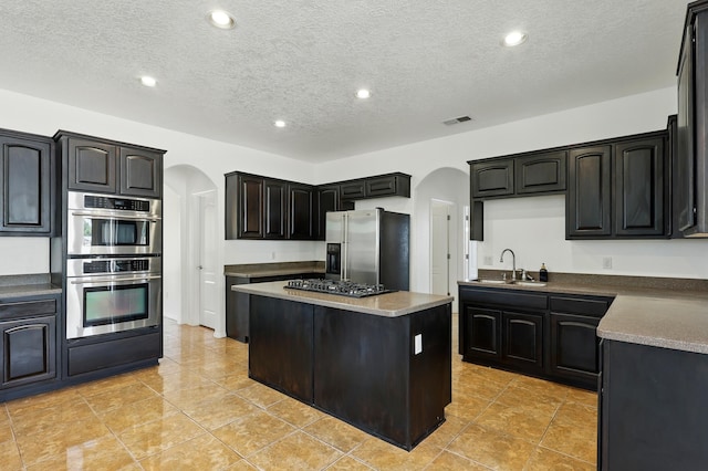 2061 Blaylock Ln NE, Los Lunas, NM 87031 - kitchen with stainless steel appliances, arched walkways, a kitchen island, a textured ceiling, and light tile patterned flooring