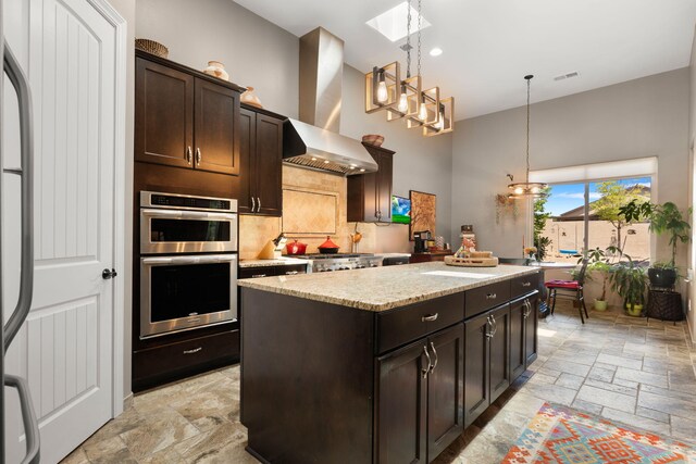 2633 Globe Ct NE, Rio Rancho, NM 87124 - kitchen featuring a towering ceiling, double oven, stone tile floors, a center island, and wall chimney exhaust hood