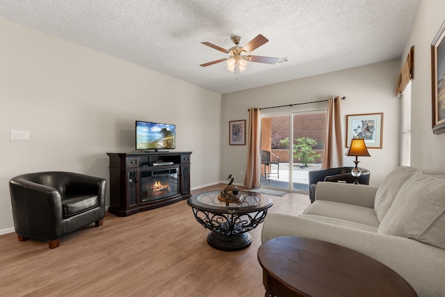 429 Paseo Vista Loop NE, Rio Rancho, NM 87124 - living room featuring light wood finished floors, a ceiling fan, a glass covered fireplace, a textured ceiling, and baseboards