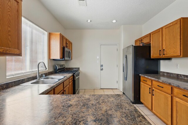 10016 Rio Canon Ave SW, Albuquerque, NM 87121 - kitchen featuring appliances with stainless steel finishes, dark countertops, light tile patterned floors, brown cabinetry, and a textured ceiling