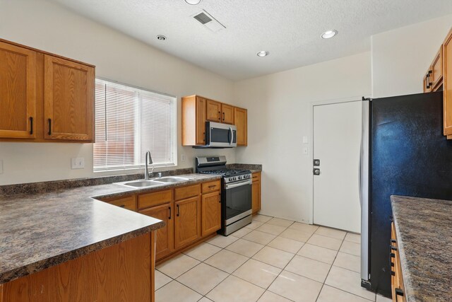 10016 Rio Canon Ave SW, Albuquerque, NM 87121 - kitchen with appliances with stainless steel finishes, dark countertops, brown cabinetry, recessed lighting, and a textured ceiling