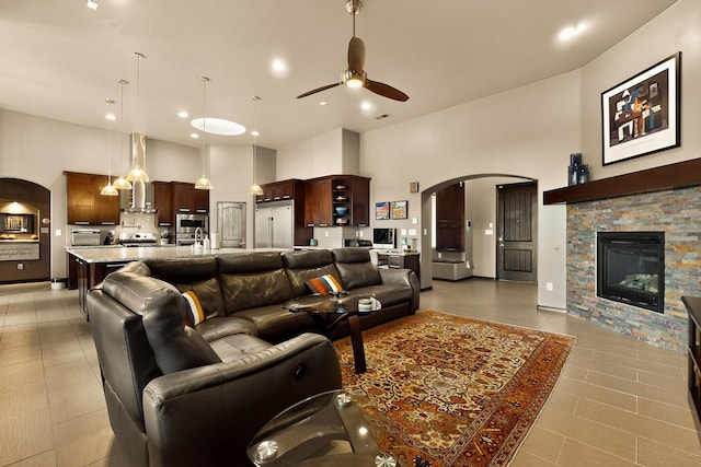 3220 Vatapa Rd NE, Rio Rancho, NM 87144 - living area featuring a ceiling fan, arched walkways, a high ceiling, a fireplace, and light tile patterned floors