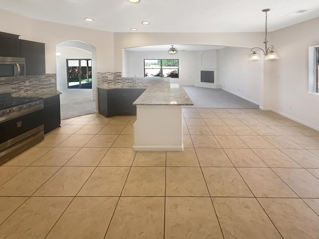 10909 Estribo St NW, Albuquerque, NM 87114 - kitchen featuring stainless steel appliances, decorative backsplash, light tile patterned flooring, light stone countertops, and a peninsula