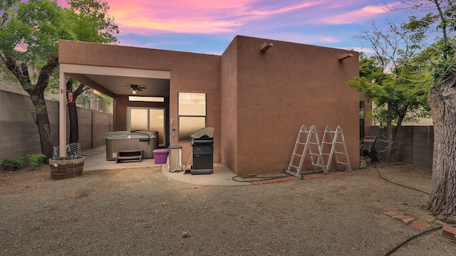 11041 Academy Ridge Rd NE, Albuquerque, NM 87111 - back of house at dusk with a hot tub, stucco siding, ceiling fan, and a fenced backyard