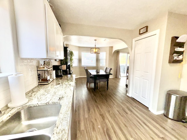 1704 Jack Nicklaus Dr, Rio Communities, NM 87002 - kitchen with arched walkways, white cabinets, light wood finished floors, decorative backsplash, and light countertops