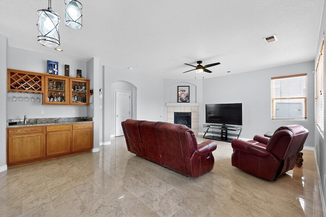1468 Montiano Loop SE, Rio Rancho, NM 87124 - living room featuring arched walkways, wet bar, ceiling fan, a tile fireplace, and light marble finish flooring