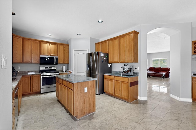 1468 Montiano Loop SE, Rio Rancho, NM 87124 - kitchen featuring stainless steel appliances, arched walkways, dark stone counters, a center island, and brown cabinetry