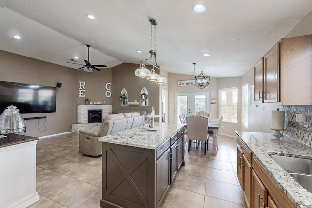 2704 Ghost Ranch St SW, Albuquerque, NM 87121 - kitchen featuring a ceiling fan, lofted ceiling, a stone fireplace, light tile patterned floors, and light stone counters