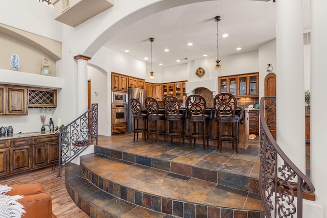 746 Chamisal Rd NW, Los Ranchos, NM 87107 - kitchen with stainless steel appliances, brown cabinets, a towering ceiling, recessed lighting, and decorative columns